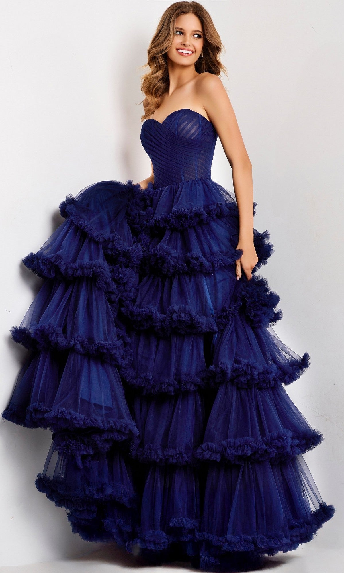 A woman models the Jovani 47139, a long dark blue strapless prom dress with elegant ruffled tiers, standing against a plain light background.